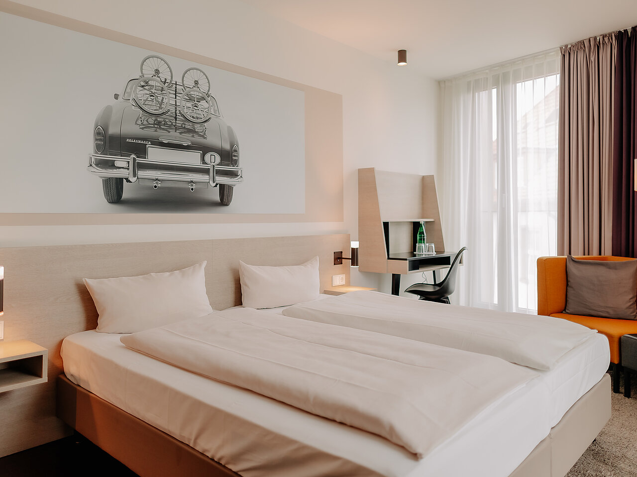 Doppelzimmer mit Arbeitsplatz im CrossINN Osnabrück Modernes Doppelzimmer im CrossINN Osnabrück mit zwei Betten, Arbeitsplatz und orangefarbenem Sessel