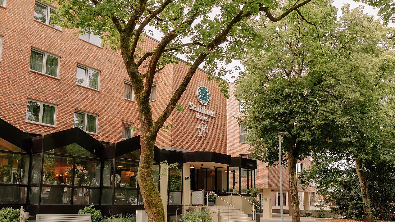 Außenansicht des Stadthotel Borken by Hackmann mit Eingangsbereich und Bäumen