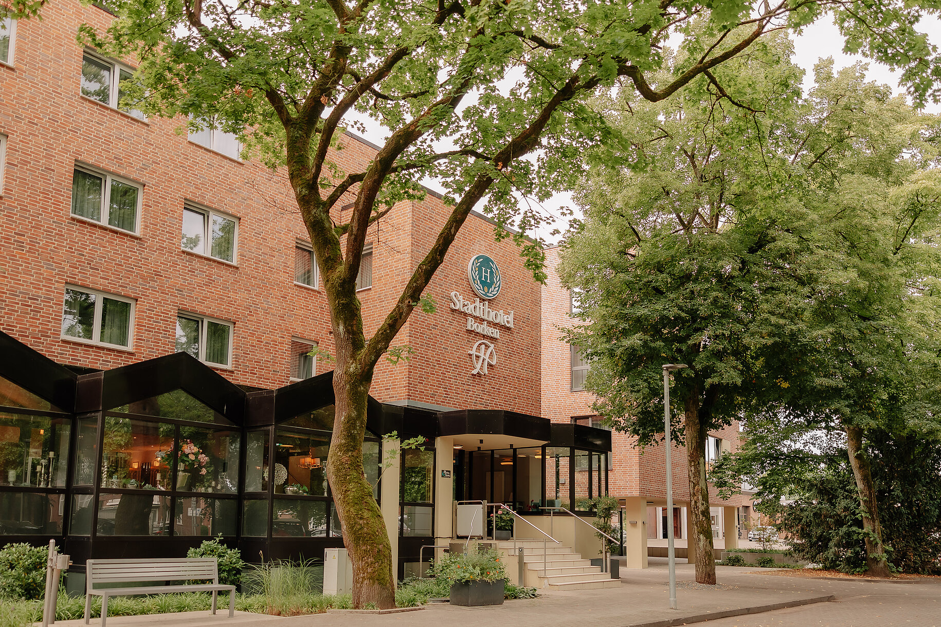 Außenansicht des Stadthotel Borken by Hackmann mit Eingangsbereich und Bäumen