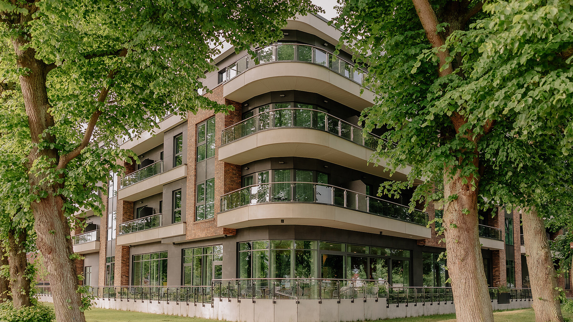 Außenansicht eines modernen Hotels mit großen Balkonen und Glasfassade, umgeben von Bäumen