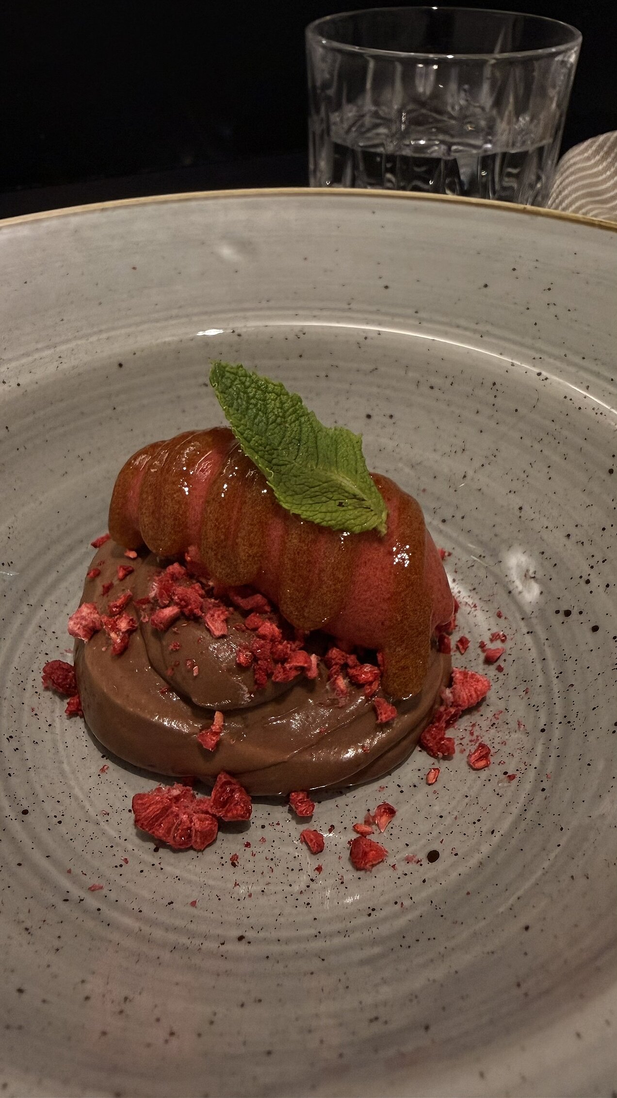 Himbeer-Rote-Beete-Sorbet mit Schokoladencréme, Malz-Bier-Gel, Himbeerpulver und Schmetterlingshippe, kunstvoll angerichtet auf einem Teller.