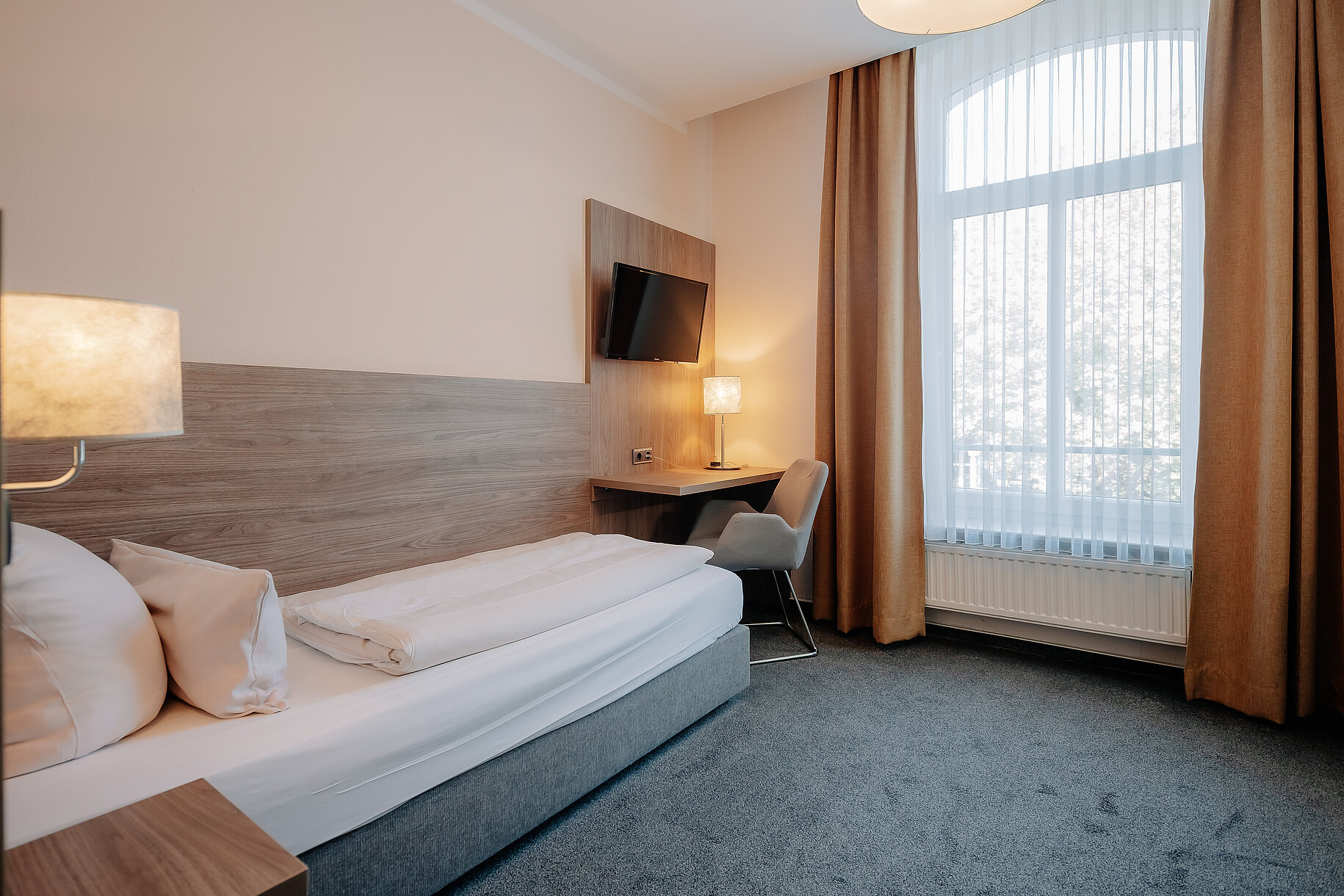 Hotelzimmer mit Bett, Schreibtisch, Fernseher und großem Fenster im Parkhotel Lingen