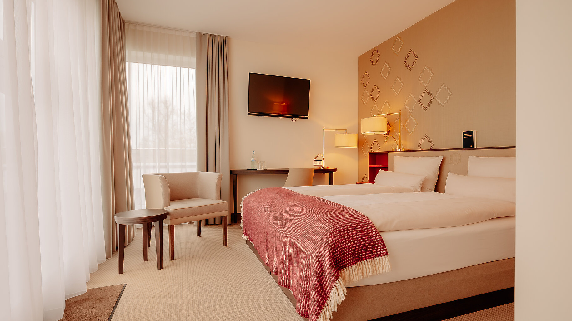 Helles Hotelzimmer mit Doppelbett, Schreibtisch und gemütlicher Sitzecke im LOOKEN INN Lingen