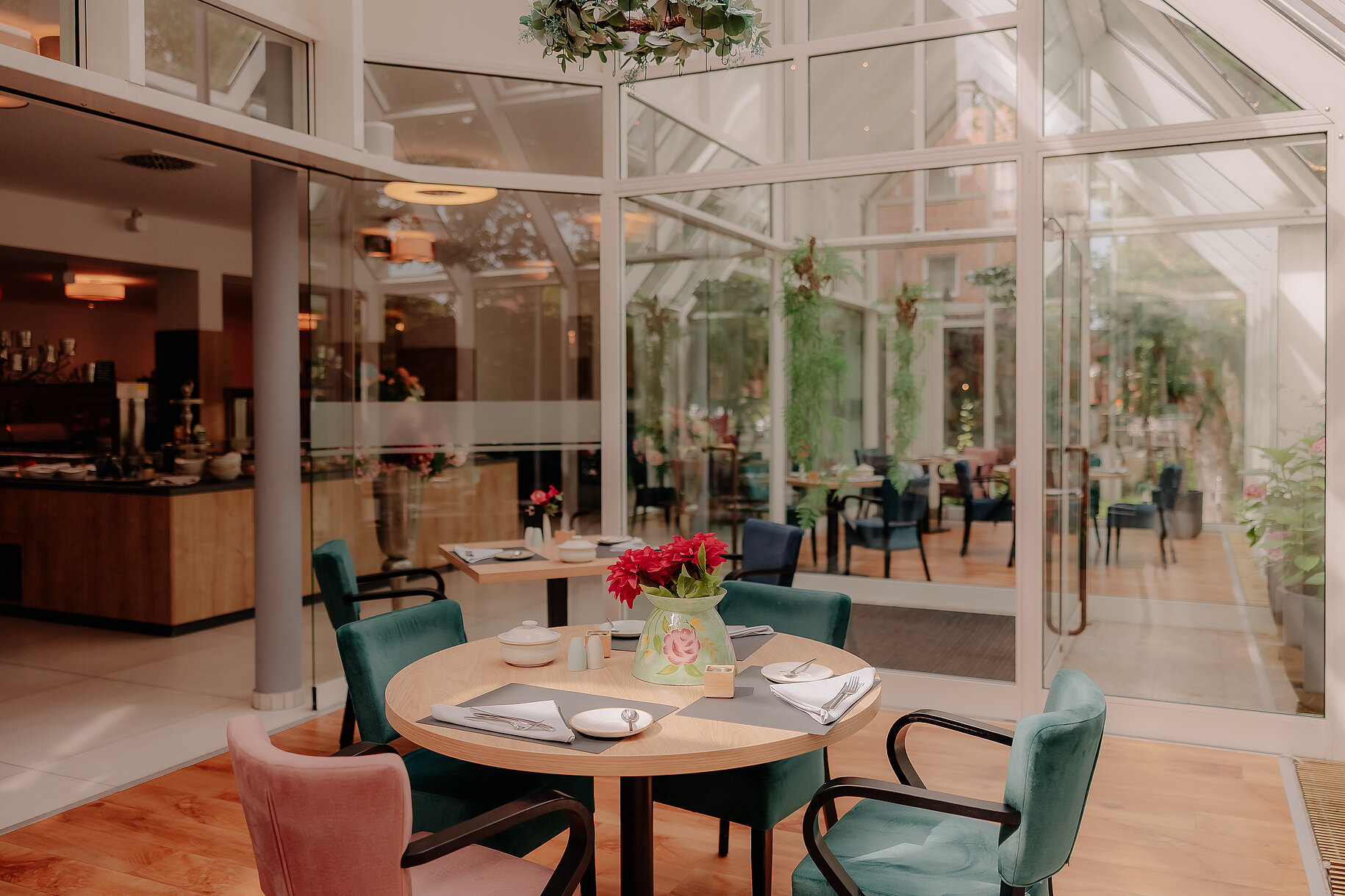 Frühstückstisch im Wintergarten des Stadthotels Borken mit bunter Dekoration und Blick auf den lichtdurchfluteten Gastraum