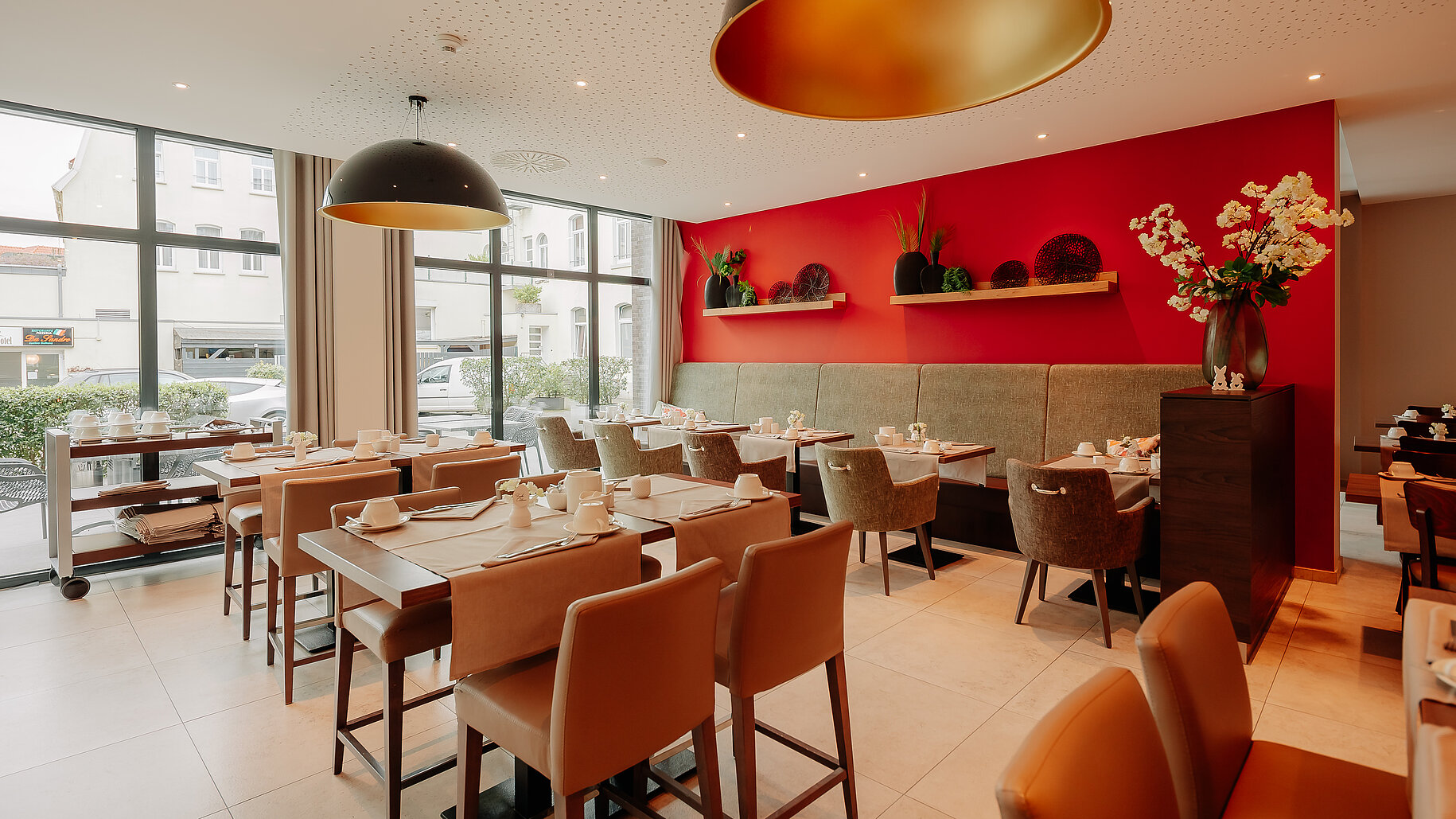 Moderner Frühstücksraum mit großen Fenstern und roter Akzentwand im LOOKEN INN Lingen