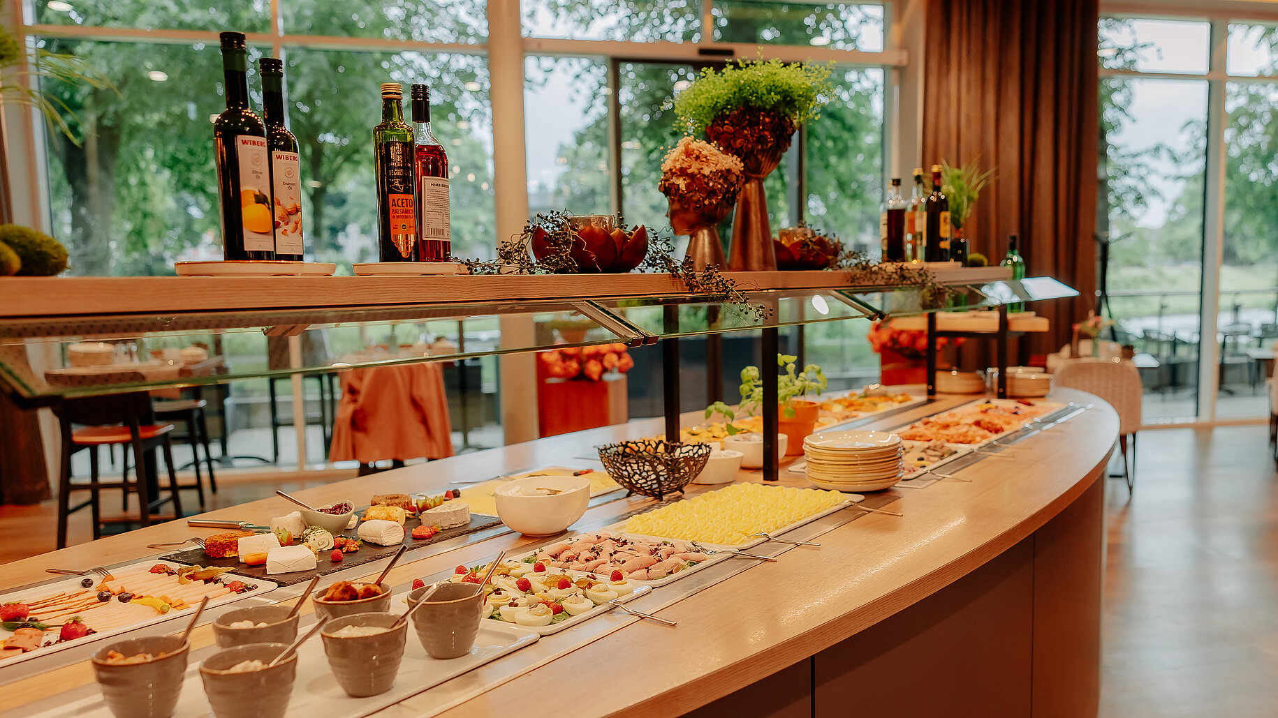 Reichhaltiges Frühstücksbuffet mit Käse, Aufschnitt, Joghurt und frischem Obst im stilvollen Restaurantbereich der Hackmann Hotels, mit Blick auf die Terrasse und viel Tageslicht