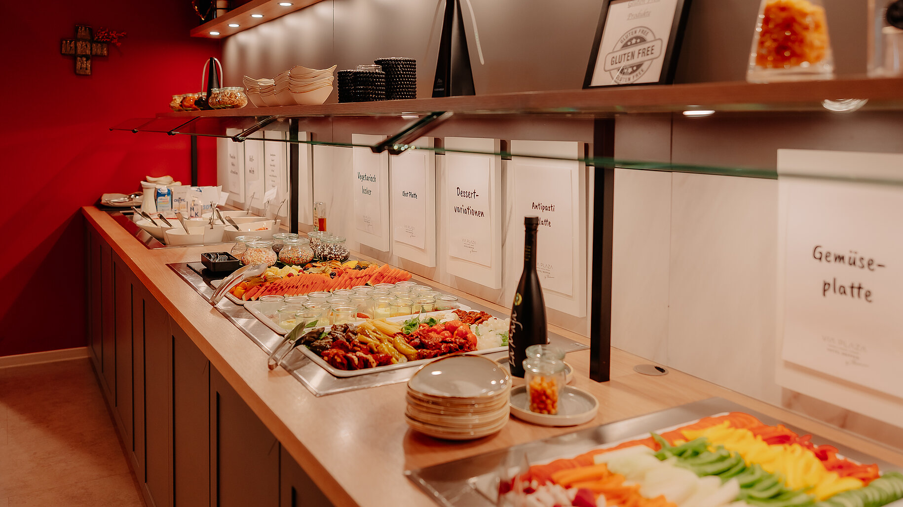 Buntes Buffet mit Gemüseplatte, Antipasti und Dessertvariationen im Frühstücksbereich mit roter Wand