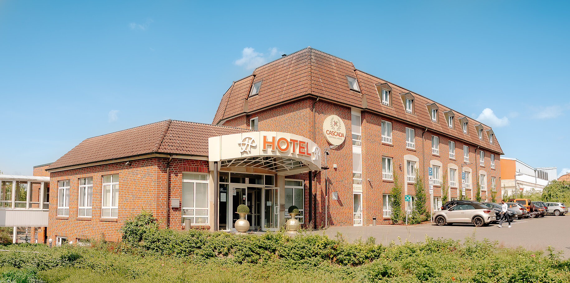 Außenansicht des CASCADA Hotels in Rheine mit Parkplatz und rotem Klinkerbau