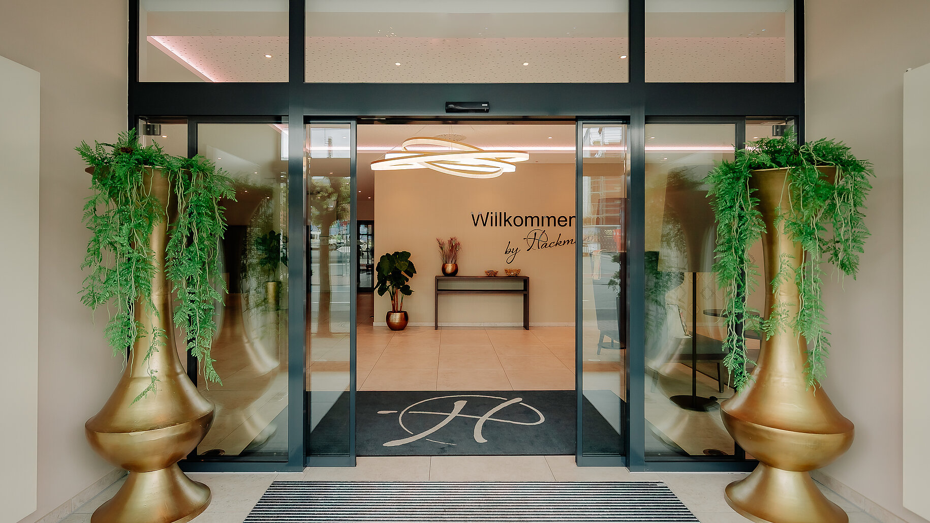 Eingangsbereich des LOOKEN INN Lingen mit automatischer Glastür und goldenen Vasen